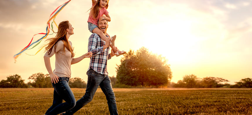 child on father's shoulders flying kite 